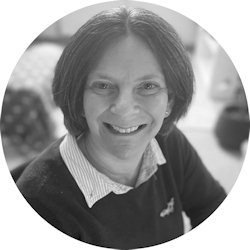 Black and white image of Cally Edwards. Cally is a white woman with bobbed, dark hair. She's wearing a white collared shirt and a dark jumper over the top. Cally shares about training as a doula and her life before doulaing!