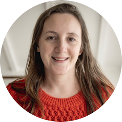 Photo of the author, Sarah Ojar, who is writing about doulas supporting families with a diagnosis of Down syndrome. Sarah is a white woman with long, straight, light brown hair. She's wearing a red/orange jumper.